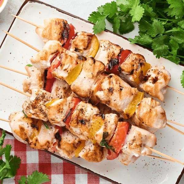 Grilled chicken and vegetable skewers with red and yellow bell peppers on a white plate.