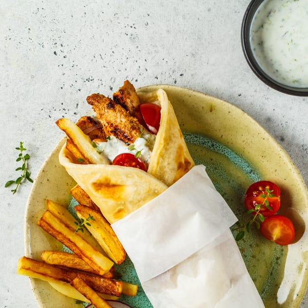 A chicken gyro with fries, cherry tomatoes, and a side of tzatziki sauce on a plate.