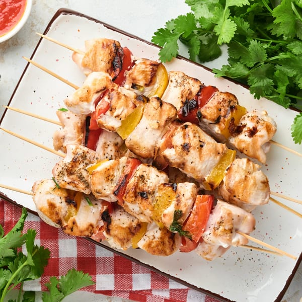 Grilled chicken and colorful bell pepper skewers on a white plate with a red checkered napkin.