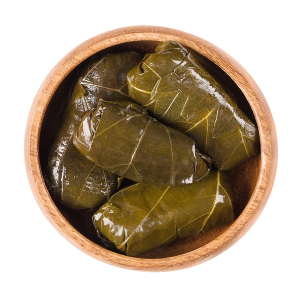 A wooden bowl filled with several green, shiny stuffed grape leaves, known as dolmades.