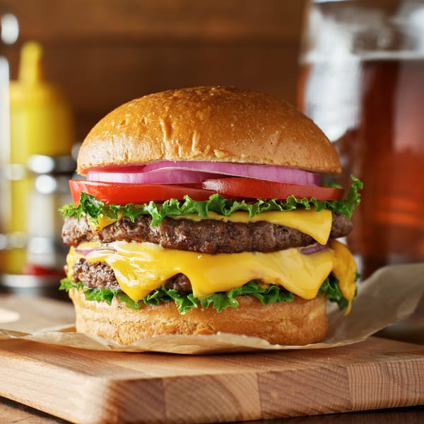 A double cheeseburger with lettuce, tomato, and red onion on a wooden board at Moody's Coney Island Diner.