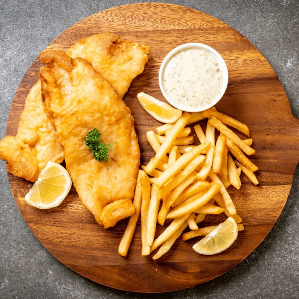 Golden-brown fish and chips with tartar sauce, lemon wedges, and parsley on a wooden board.