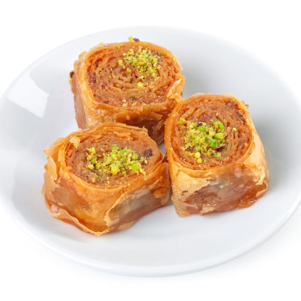 Three pieces of baklava, rolled and topped with chopped pistachios, on a white plate.
