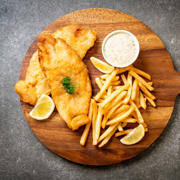 Golden-fried fish and chips with tartar sauce and lemon wedges on a wooden board.